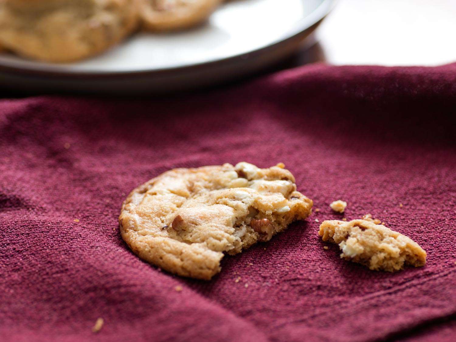 A malted chocolate chip-pecan cookie has been liberated from the plate and sampled. The half-eaten evidence lies strewn on a burgundy napkin.