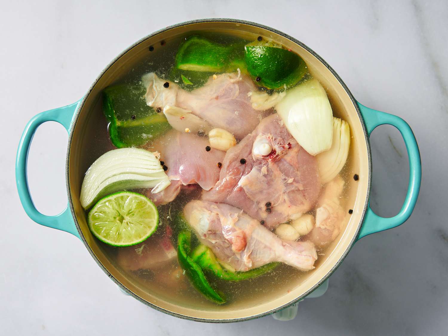 Chicken, onion, bell pepper, garlic, salt, peppercorns, and 2 quarts cold water with lime juice and lime halves in a Dutch oven.