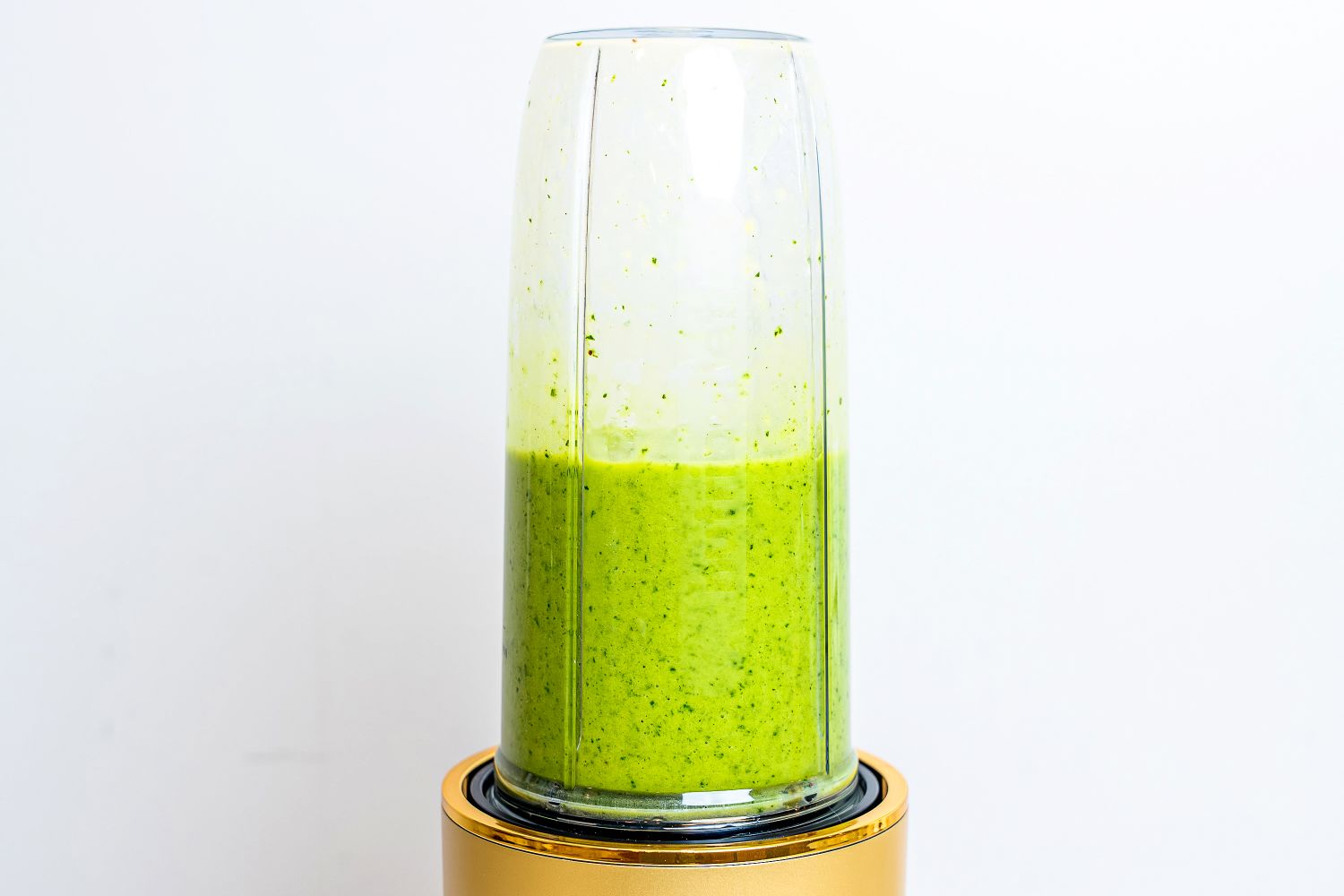 A blender blending a green smoothie on a golden base