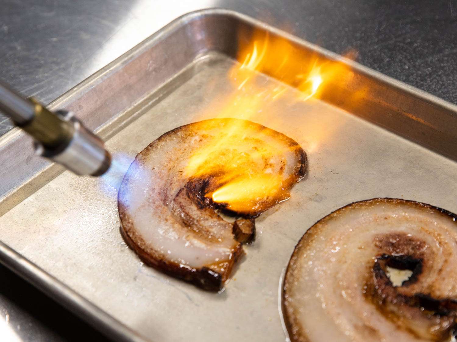 Browning slices of cooked pork belly with a blowtorch.