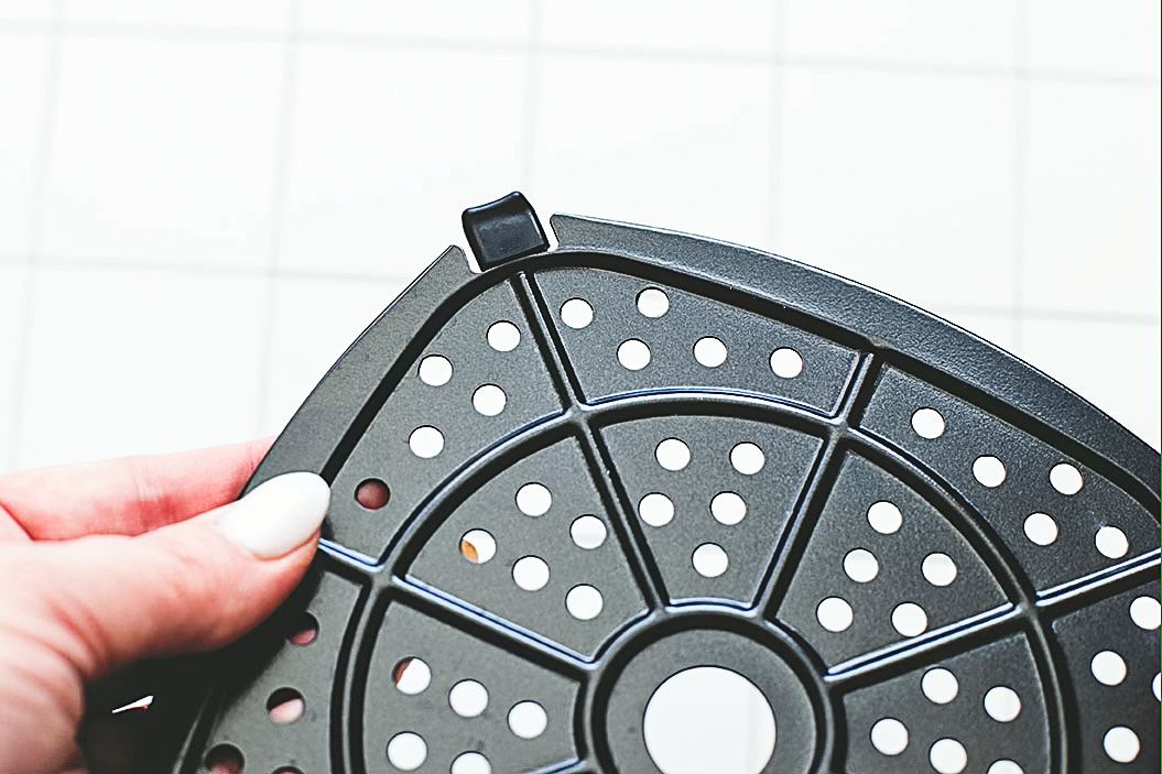 A hand holding a perforated circular plastic object