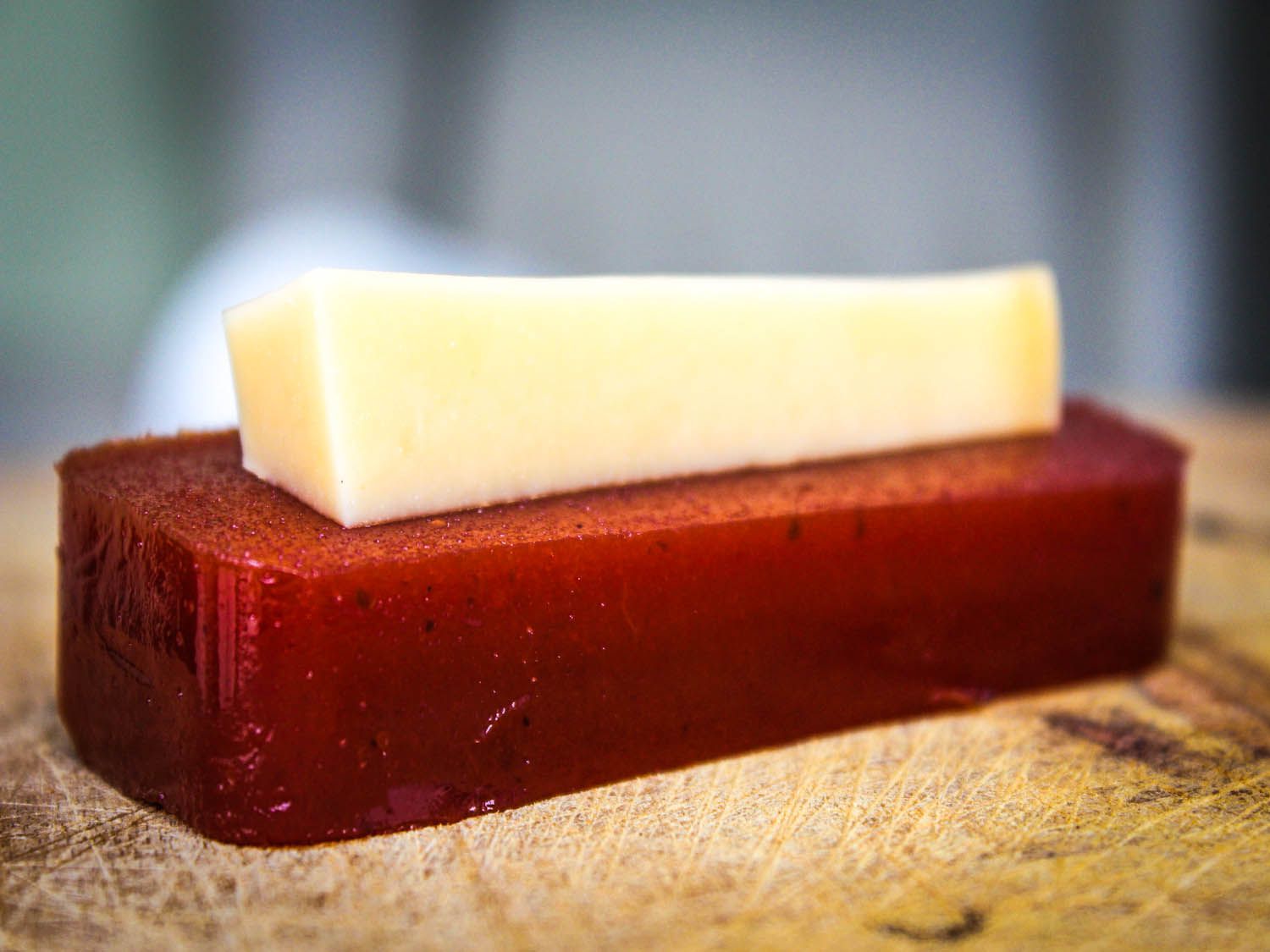 A piece of dulce de guayaba, topped with a piece of cheese on a wooden board.