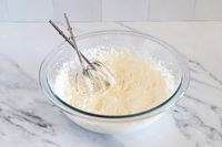 A Pyrex mixing bowl containing whipped cream with a pair of beaters resting inside