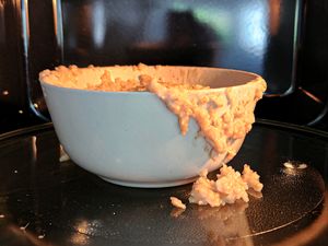 A bowl with spilled oatmeal placed on a microwave tray