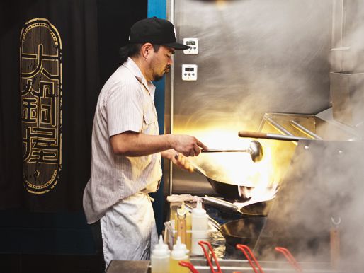 A cook making a stir-fry at a large wok.