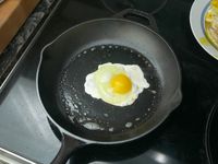 A fried egg cooking in a cast-iron skillet on a stovetop