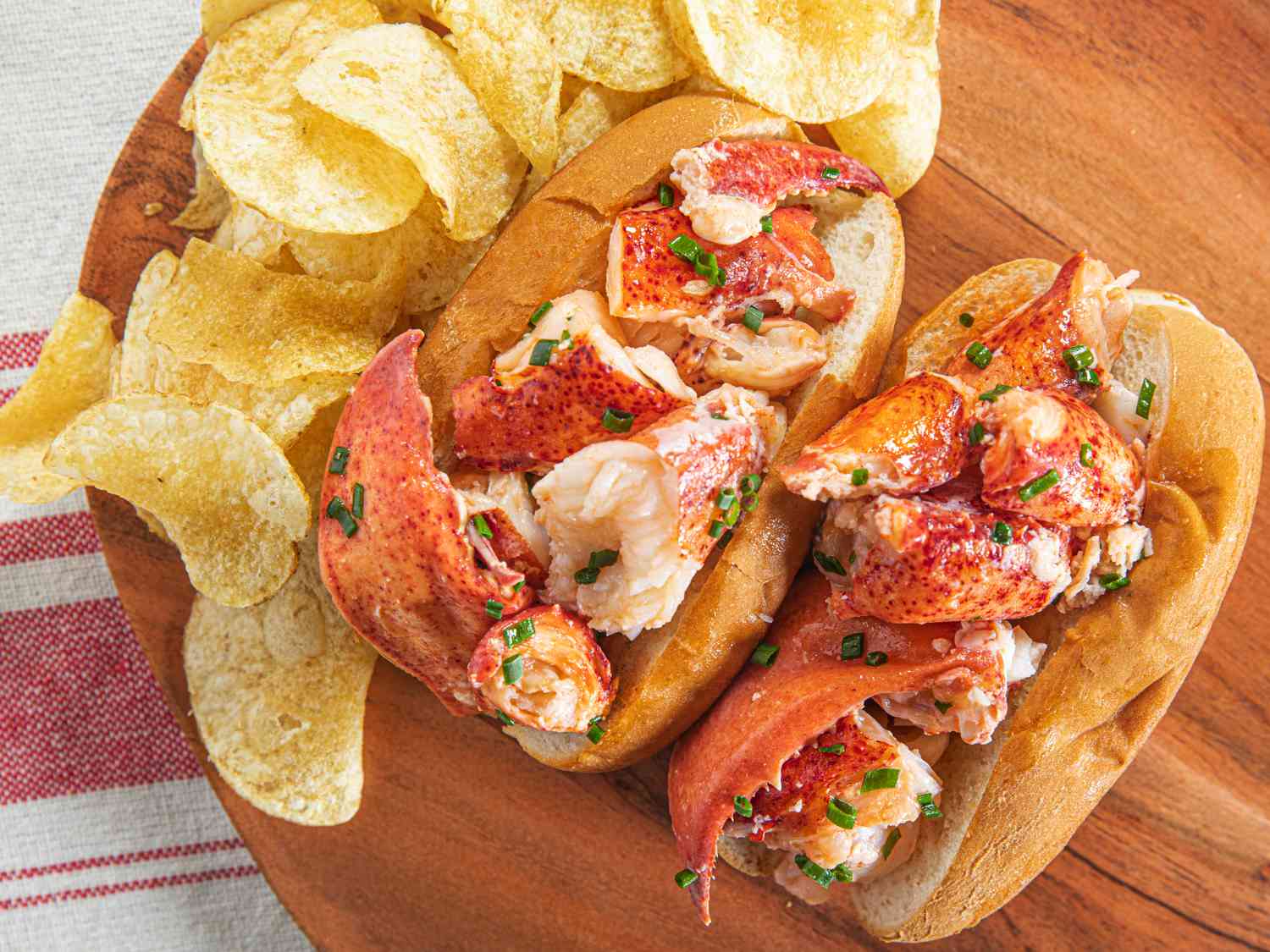 Overhead view of two lobster rolls on a wooden plate with potato chips
