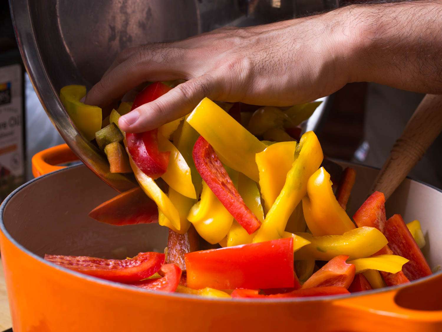 Pouring sliced bell peppers from the mixing bowl into a Dutch oven.