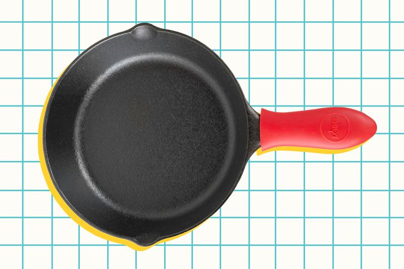 A small skillet with a red handle resting on a gridpatterned surface