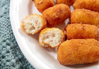 Plate of croquetas with one broken open showing the filling inside