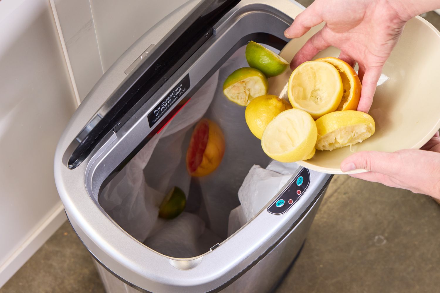 A person throws food waste into the iTouchless 13-Gallon Oval Stainless Steel Sensor Trash Can