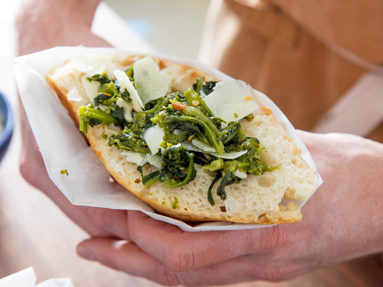 Closeup of hands holding a finished trapizzino filled with broccoli rabe.