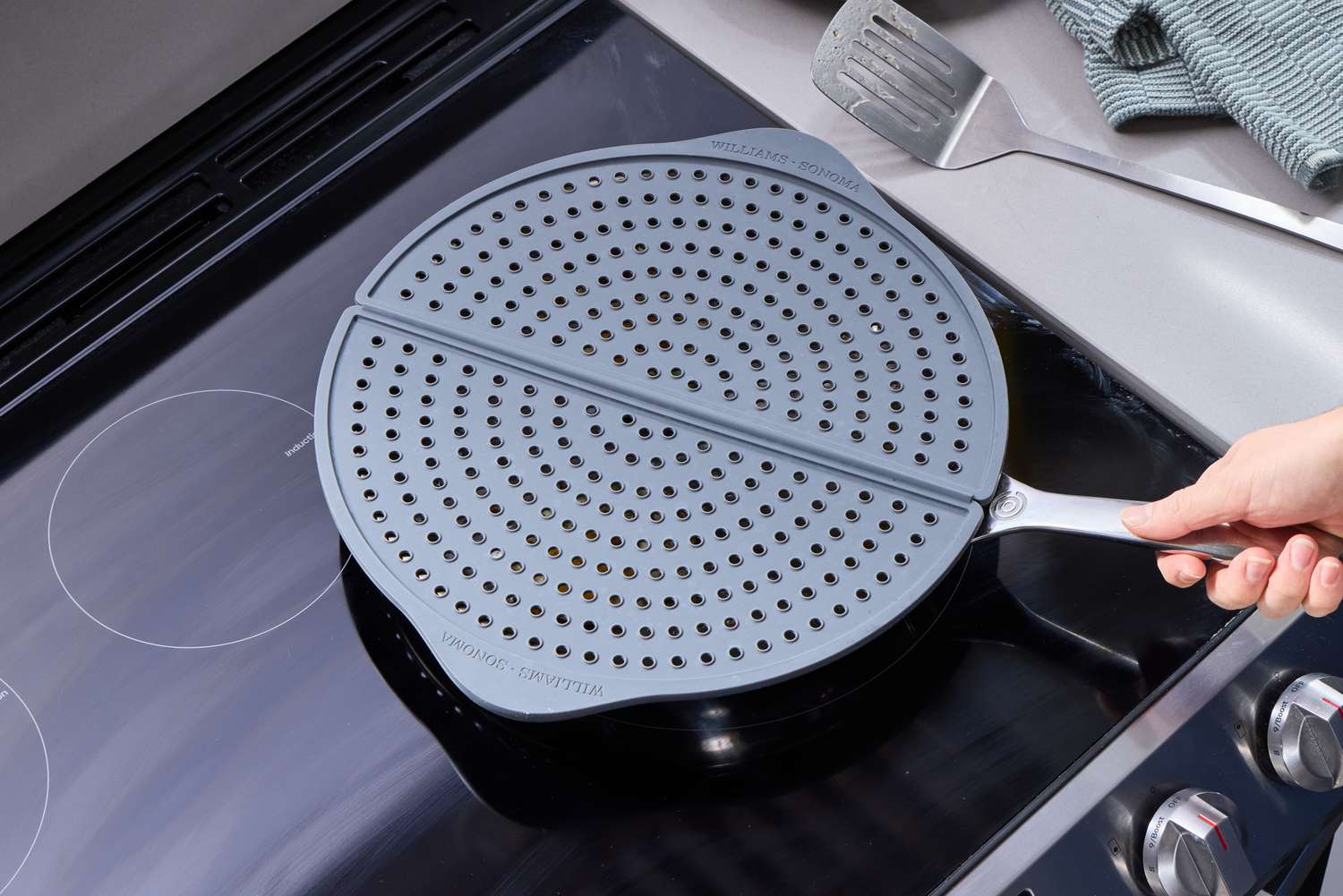 a person holding a pan with the williams sonoma splatter screen on top