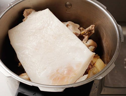 A slab of fatback resting on a pile of bones in a stockpot.