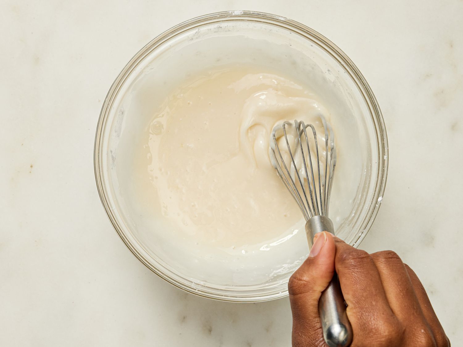 whisking glaze together in glass bowl on marble surface 