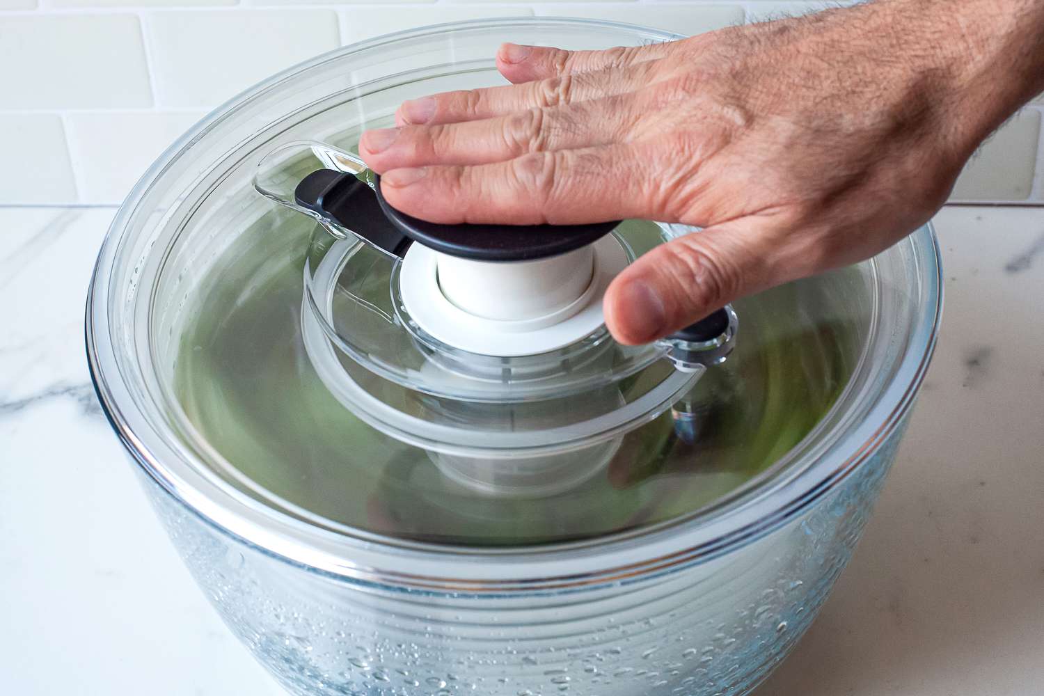 a person pumping the oxo glass salad spinner
