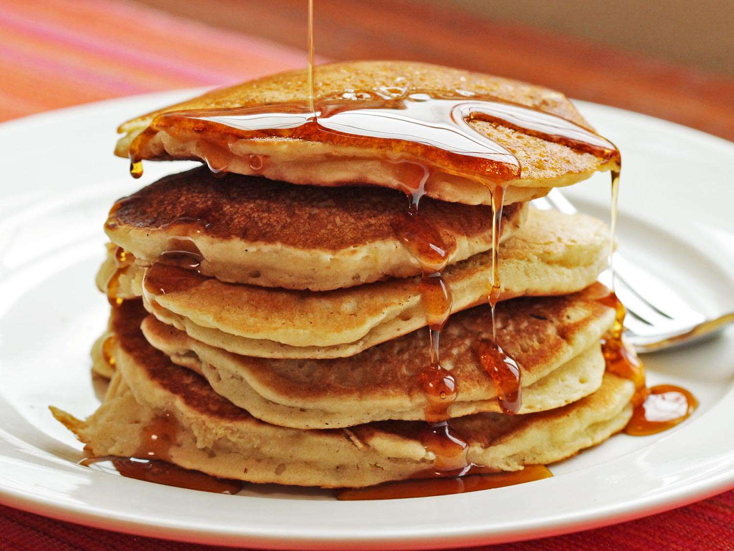 Maple syrup drizzling onto a plated stack of vegan pancakes made with aquafaba.