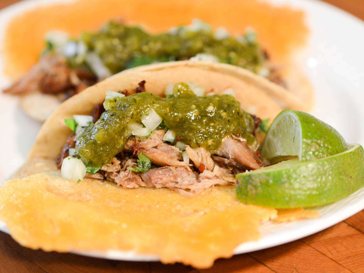 Side view of crispy parmesan taco with meaty carnitas, topping it with salsa verde, onions, and cilantro.