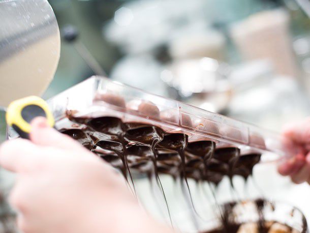 Tapping off the remaining excess melted chocolate from a bonbon mold being held upside down.