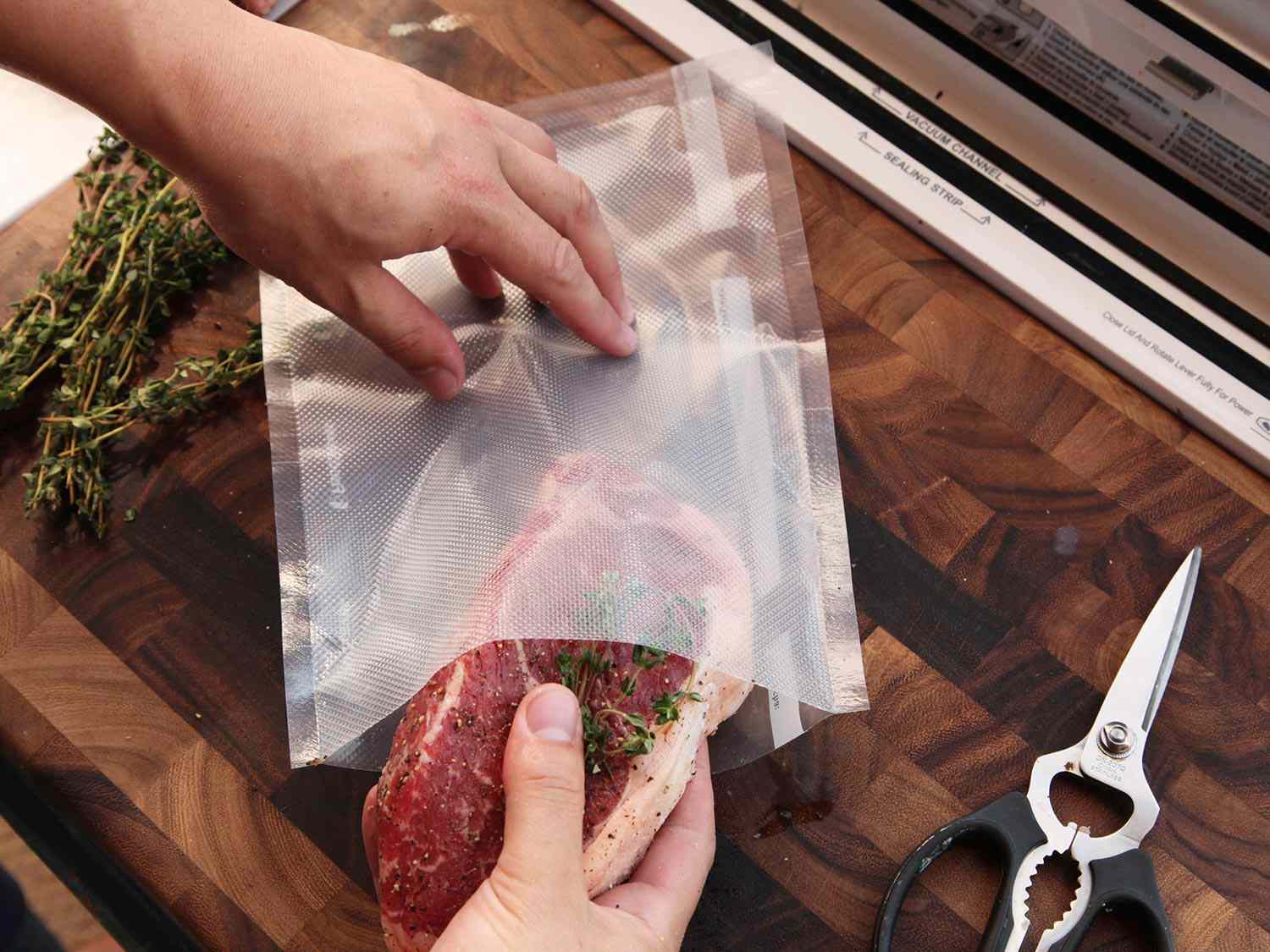 Overhead of a seasoned steak being placed in a sous vide bag with aromatics. 