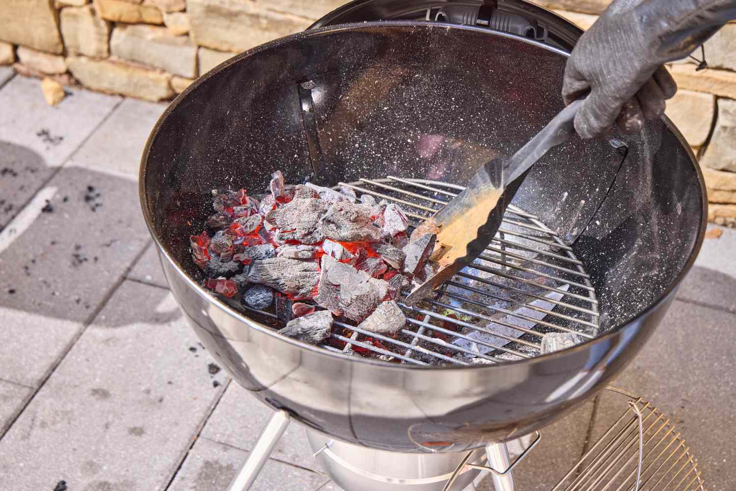 A gloved hand moving hot coals in the Weber Original Kettle Premium 22-Inch Charcoal Grill