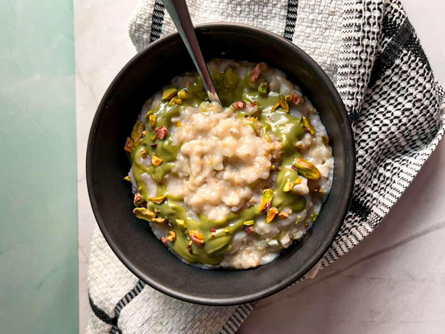 Oatmeal topped with pistachio cream and pistachios in a dark bowl with a spoon