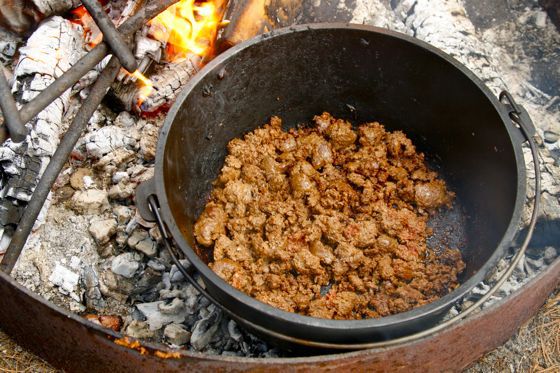 Adding sausage to a Dutch oven set over coals in a campfire.