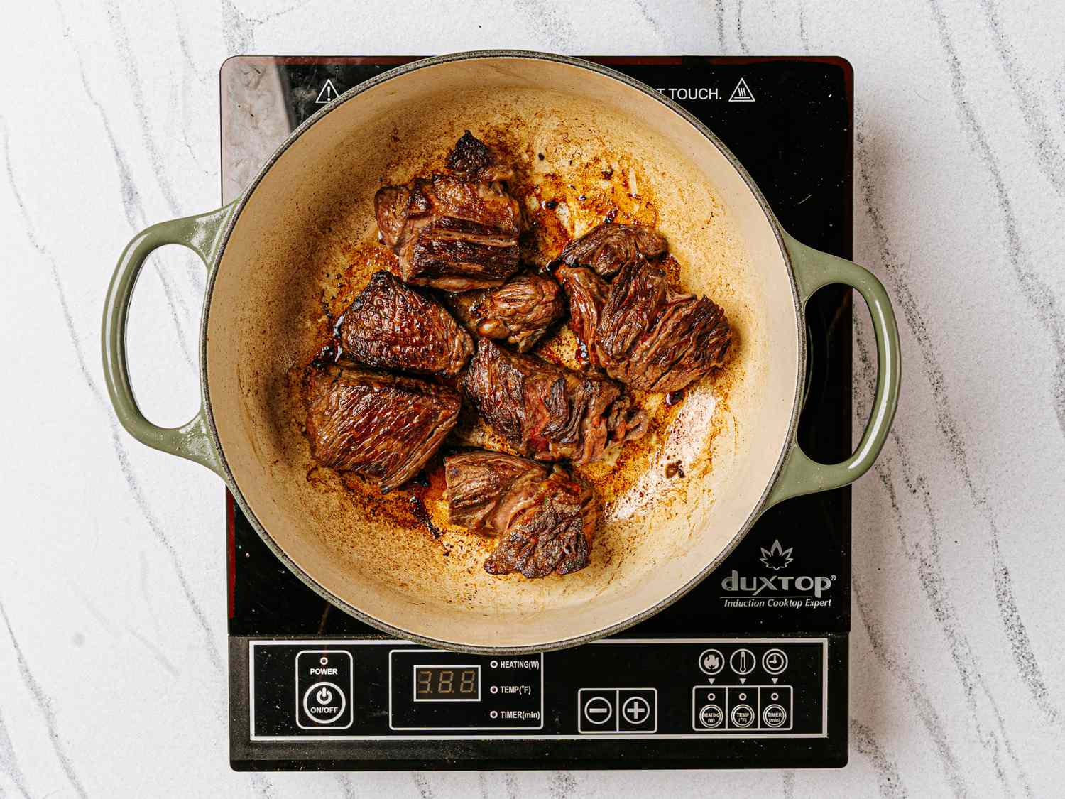 Cubed beef browning in a cast iron pot on an induction cooktop