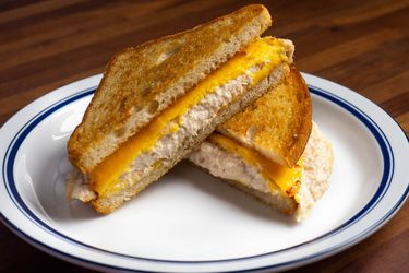 A tuna melt sandwich on a plate, cut in half diagonally to make triangles; showing melted yellow American cheese slices on top of a creamy tuna salad and nicely toasted bread.