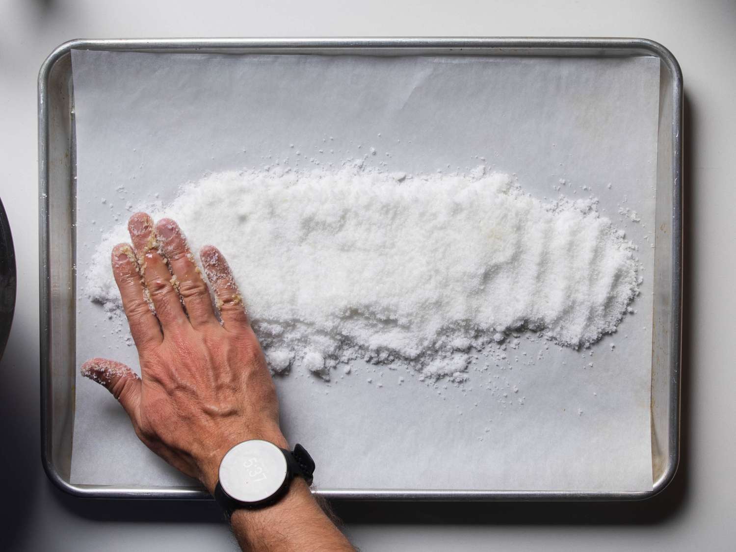 A bed of salt is spread out on a parchment-lined rimmed baking sheet, roughly in the shape of the whole fish but slightly larger.