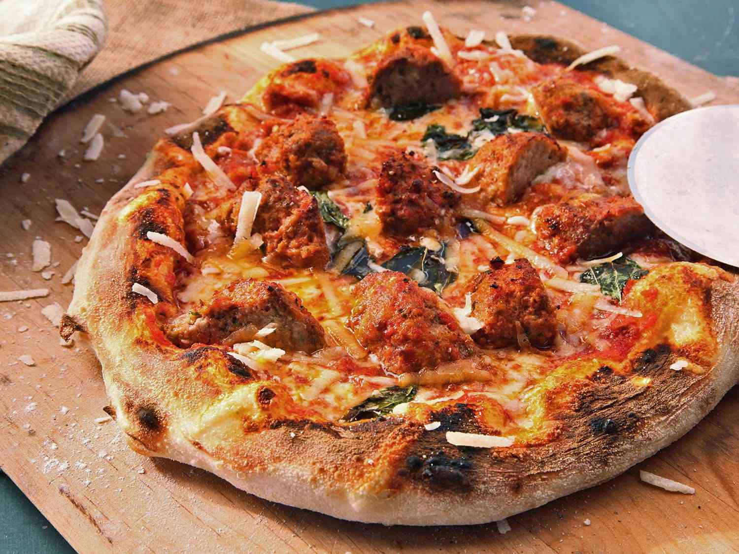 A small pizza topped with quartered large meatballs, on a wooden surface.