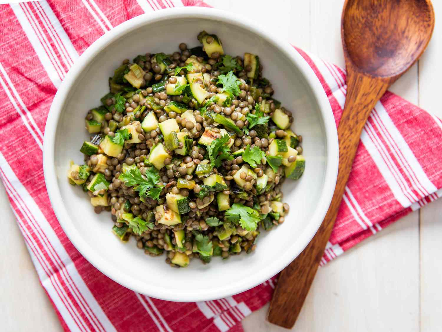 Overhead shot of a bowl of smoky lentil salad with zucchini and poblano peppers with a wooden spoon in the side