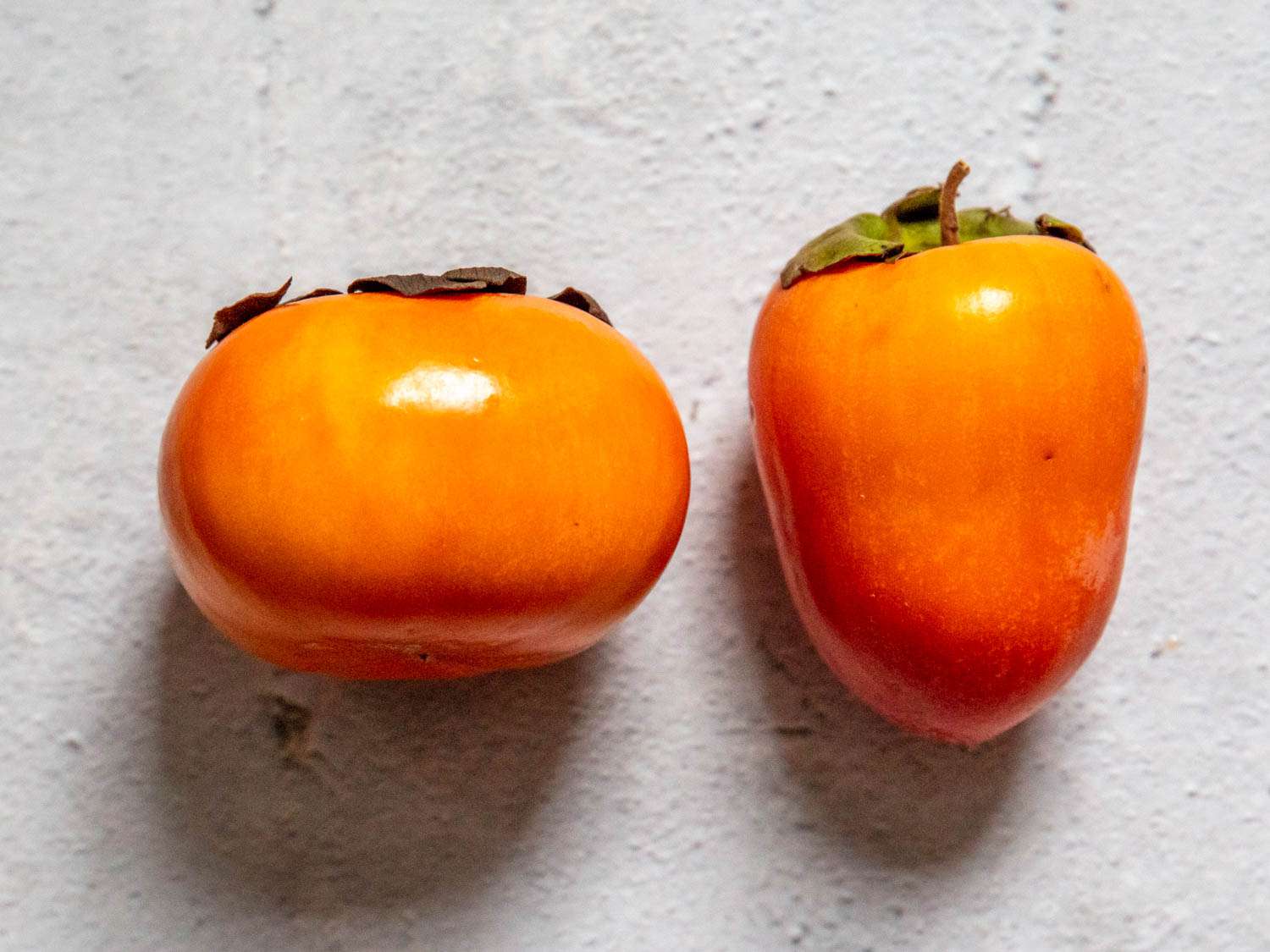 On the left: a fuyu persimmon. On the right, a tsurunoko persimmon.