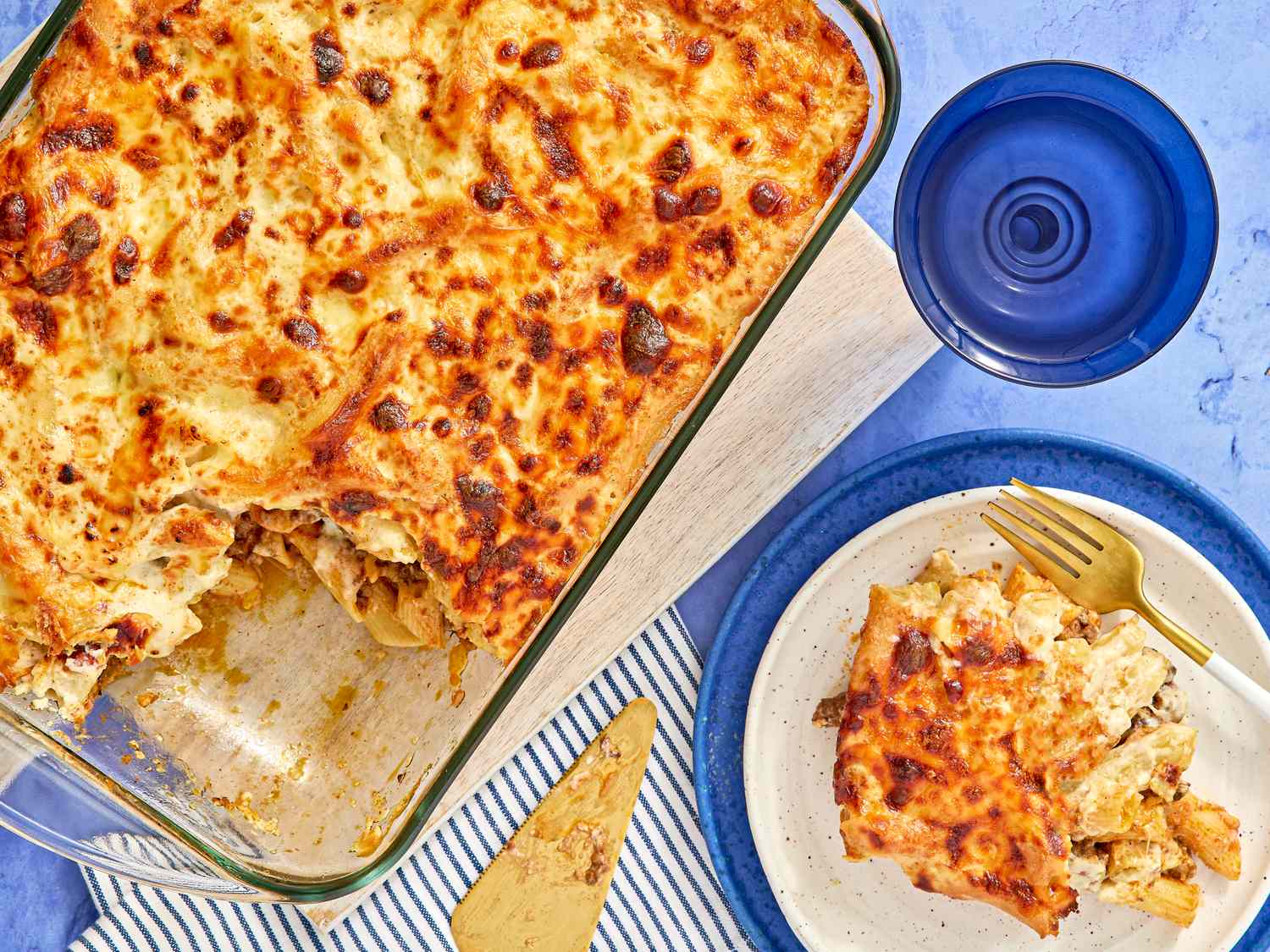 A baked pasta casserole in a glass dish with a portion served on a plate beside it