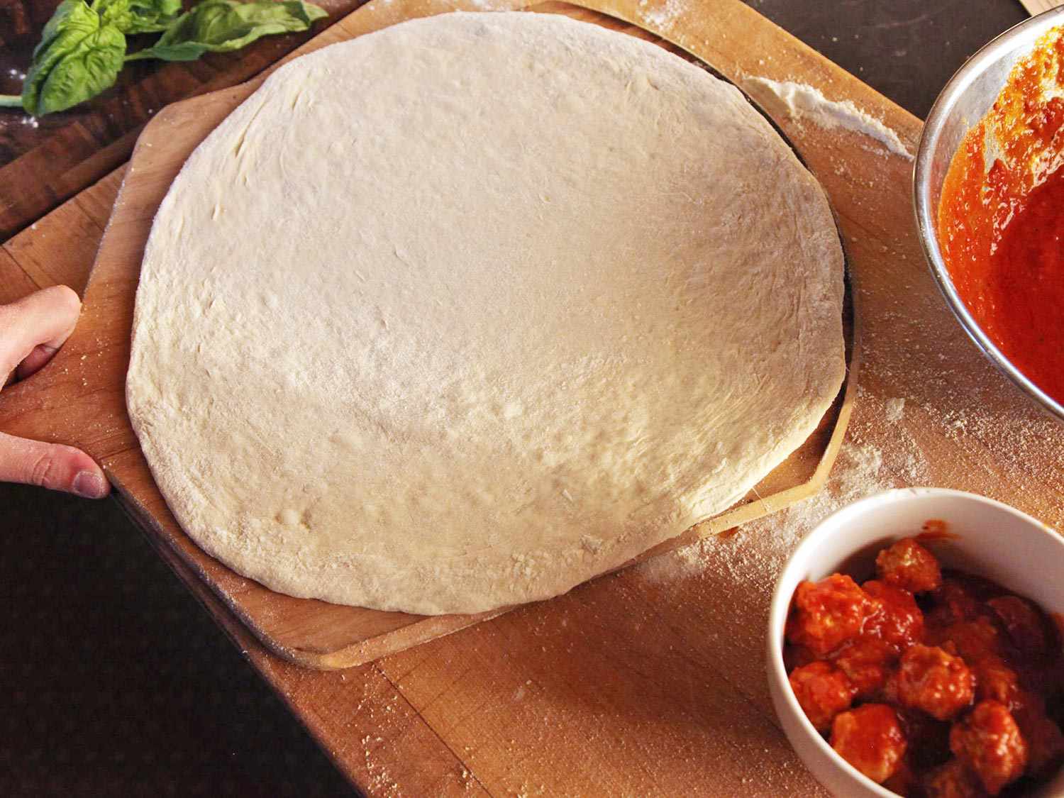Unbaked pizza dough spread out on a wooden pizza peel