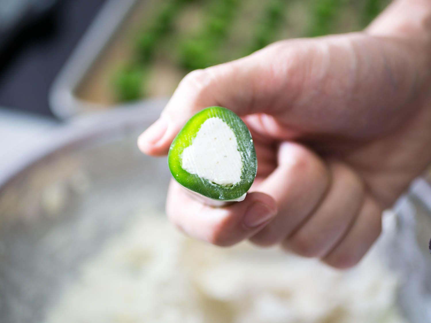 A filled jalapeño ring is held up for the camera.