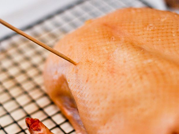 Pricking the skin of the duck with a bamboo skewer.