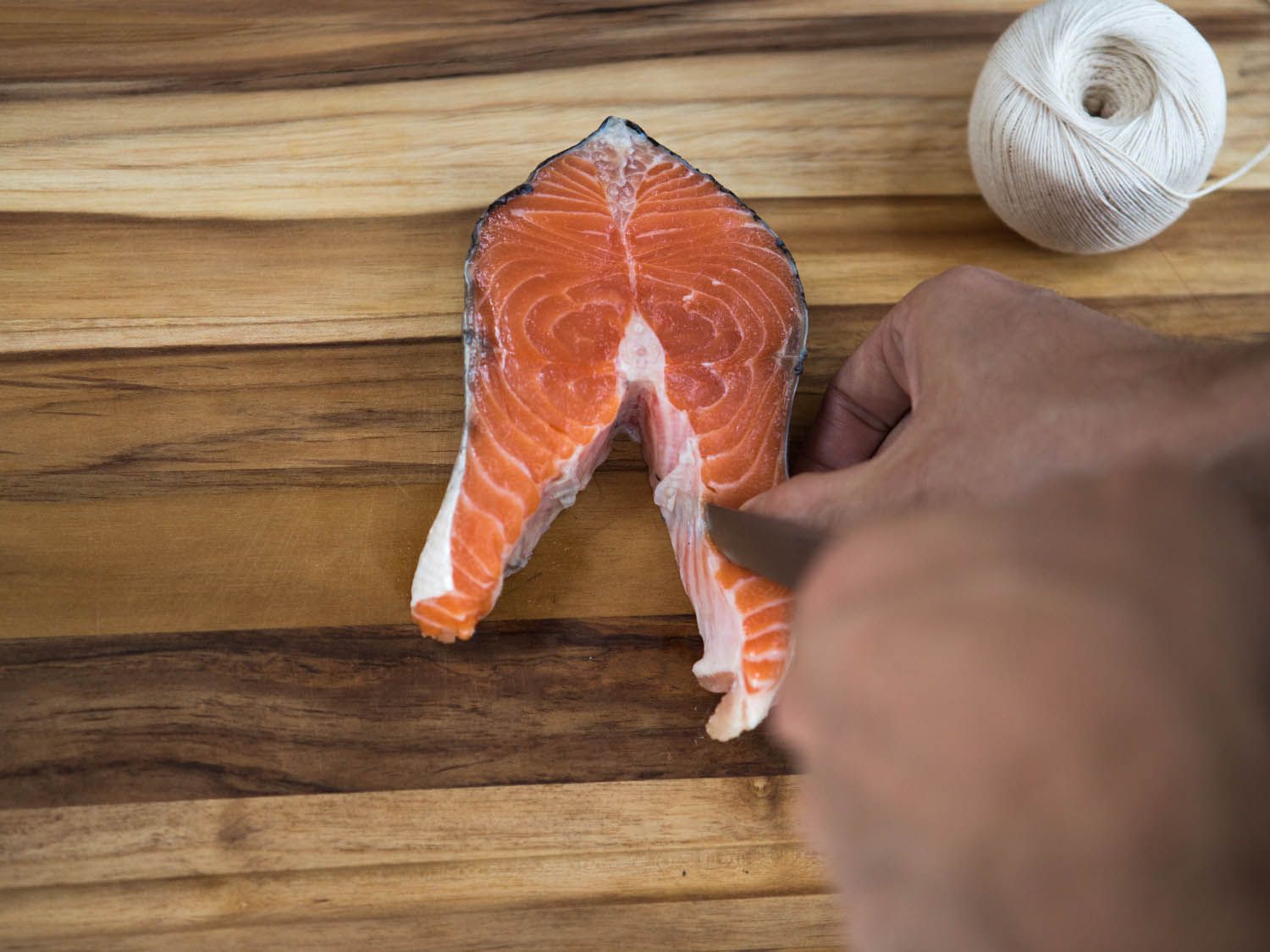 Trimming a salmon steak on a wooden board. A roll of twine is off to the side.
