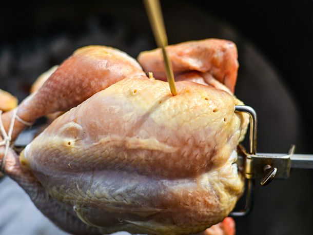 The dry-brined chicken, skewered on the rotisserie spit, is perforated in the fatty area with a bamboo skewer.