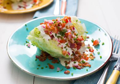 A loaded wedge salad on a light blue plate with a fork and knife off to the side