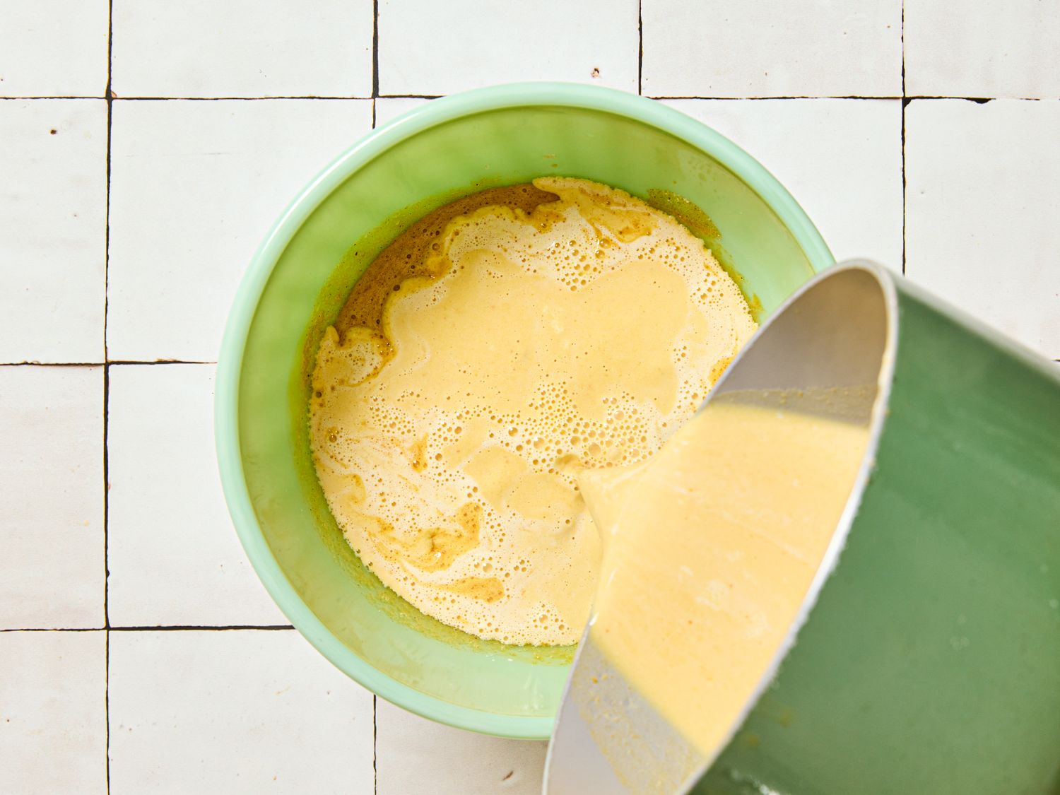 Custard mixture being poured into a bowl seen on a tiled surface