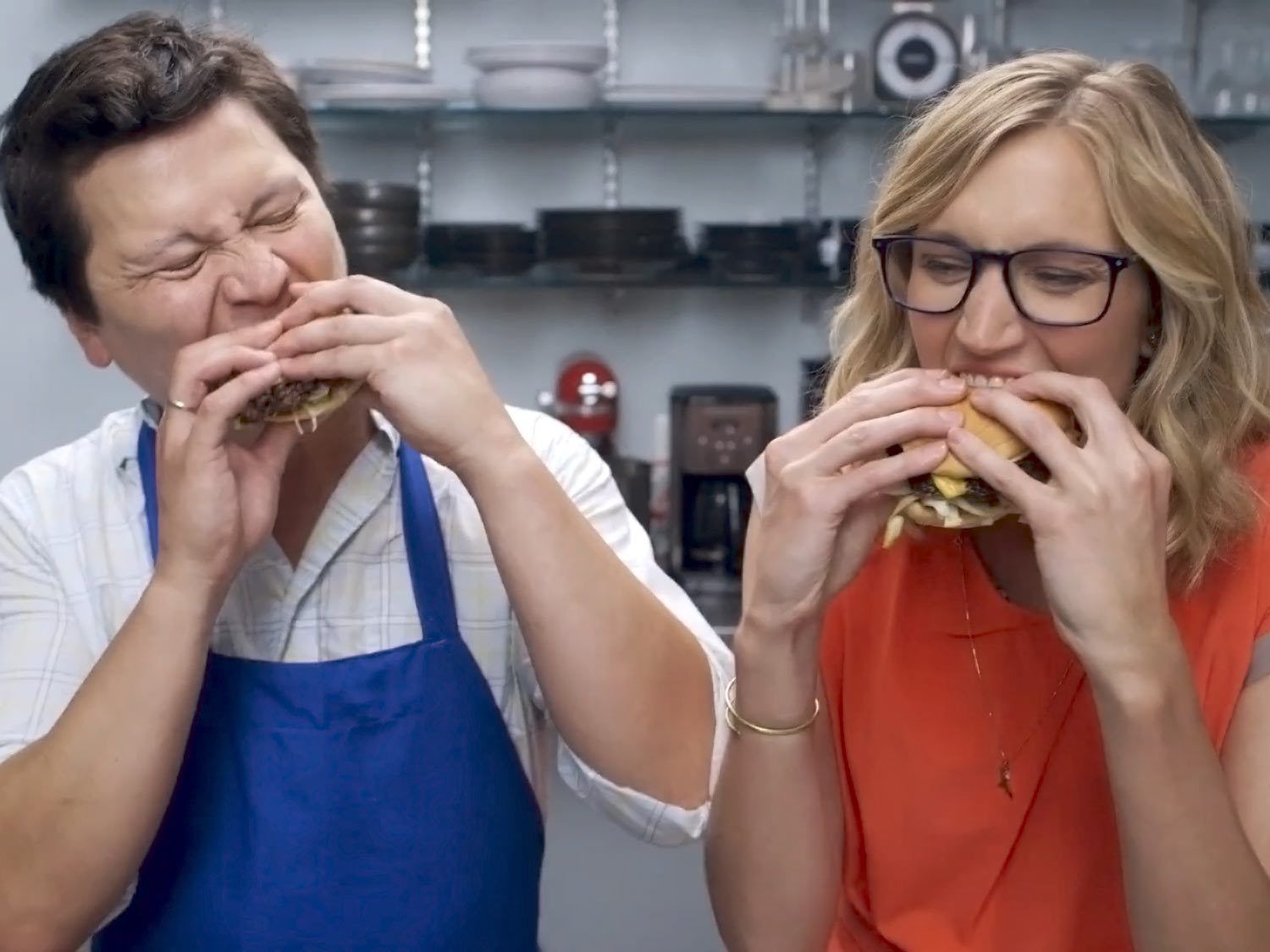 Kenji Lopez-Alt and Katie Quinn side by side stuffing their faces with cheeseburgers