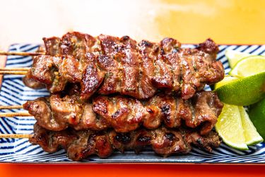 Thai-style grilled pork skewers on a rectangular platter with lime wedges 