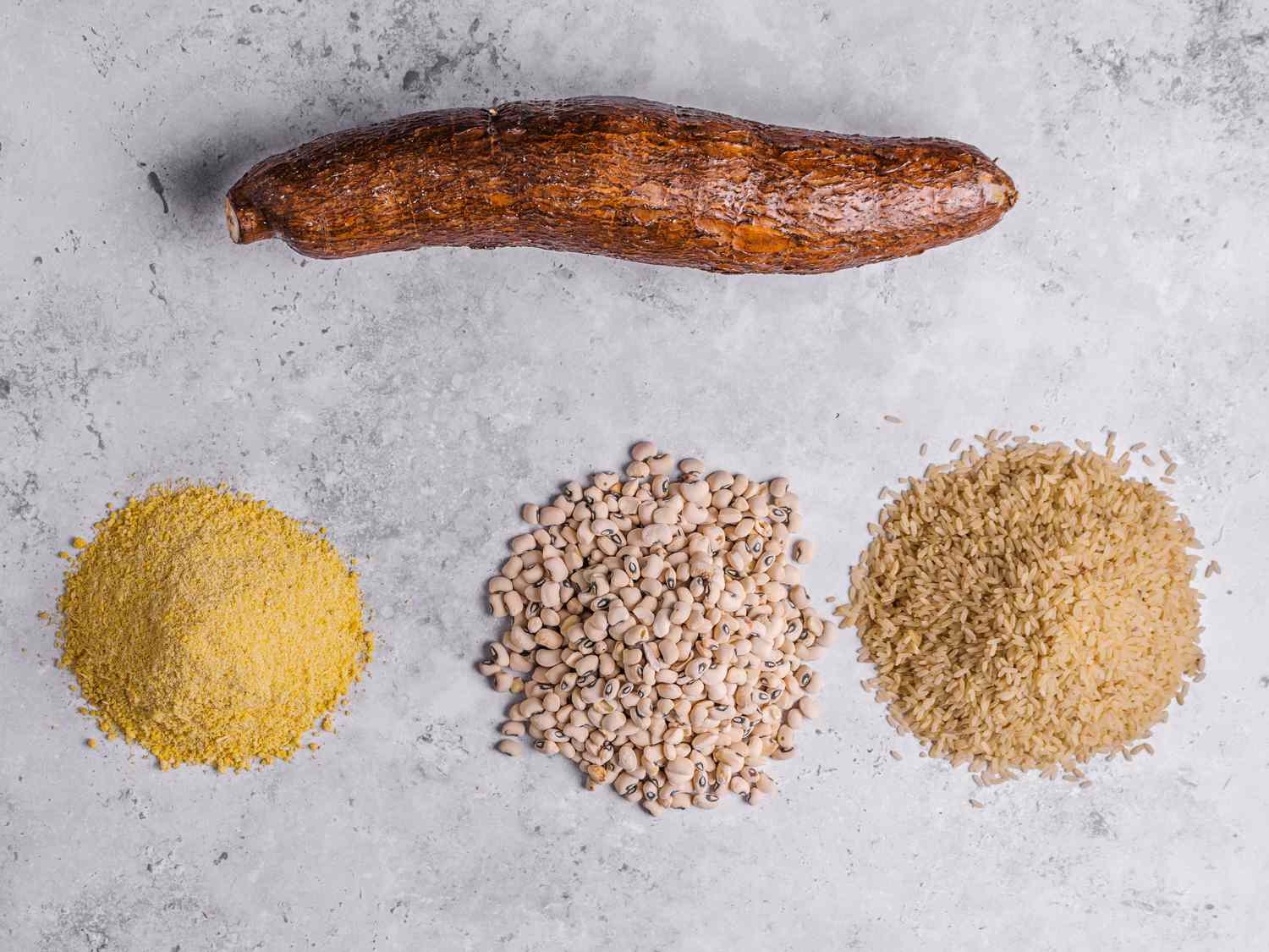 Top down view of cassava, rice, black-eyed beans, and gari on a marbled grey surface