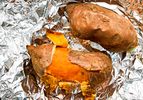 Two roasted sweet potatoes on foil one partially peeled to expose the orange flesh inside