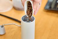 A person pours coffee beans into the Timemore C2 Max Manual Grinder