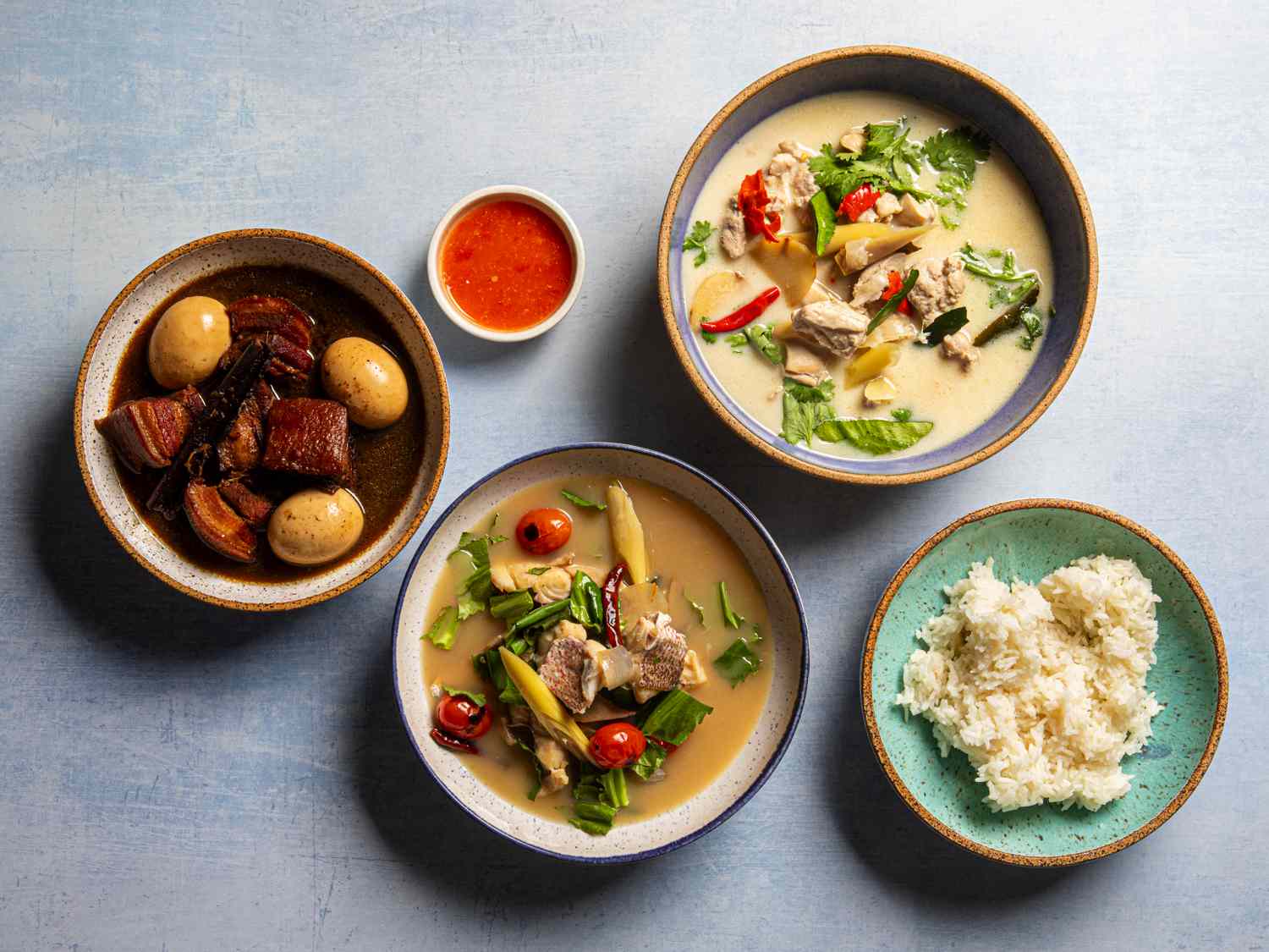 Overhead view of three Thai soups with rice and dipping sauce.
