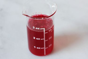 A 3 oz beaker filled with vivid red cranberry syrup.