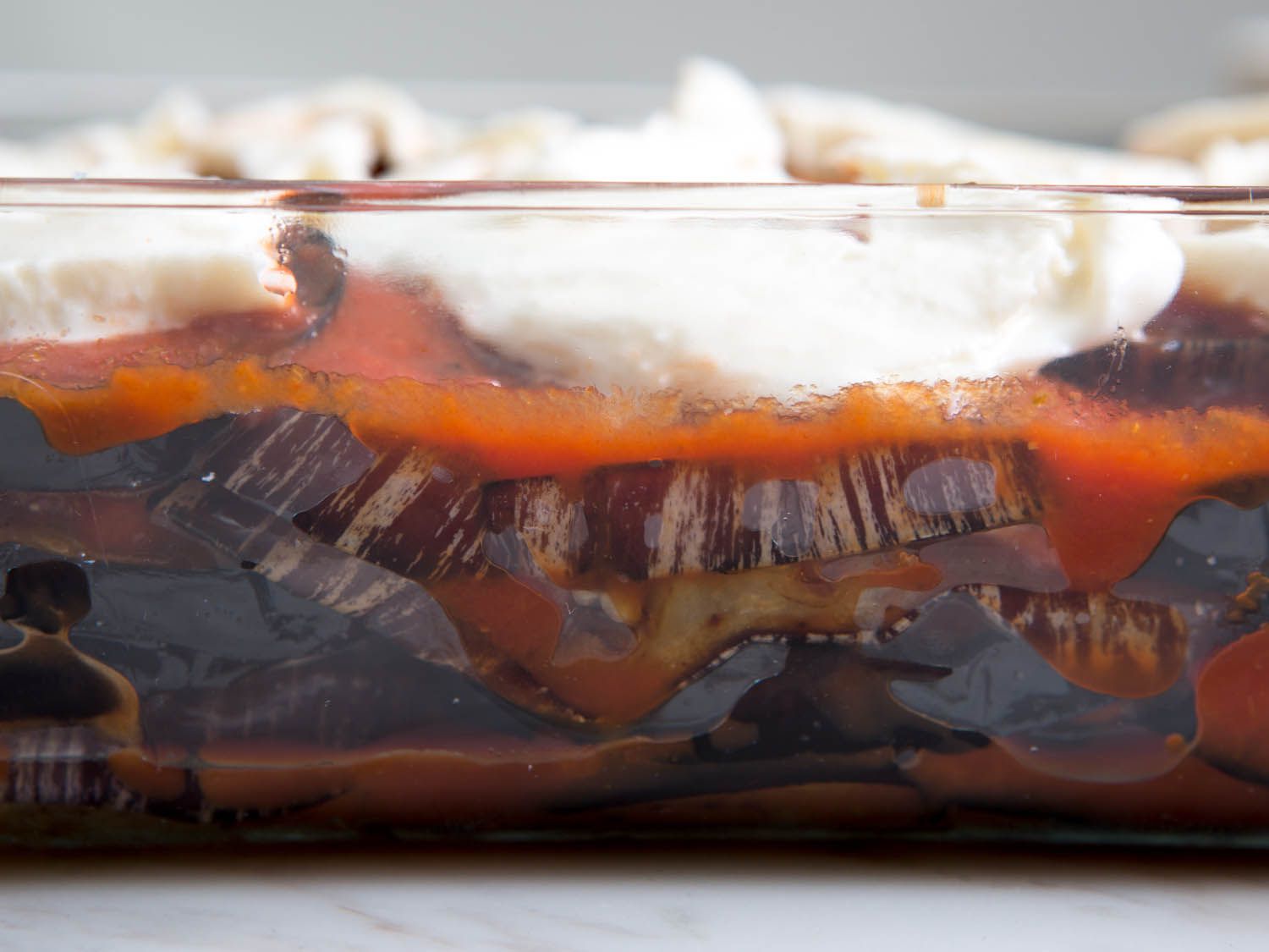 A side view of layered eggplant, sauce, and cheese in a baking dish.