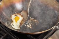 A person cooks an egg in the Joyce Chen Carbon Steel Wok